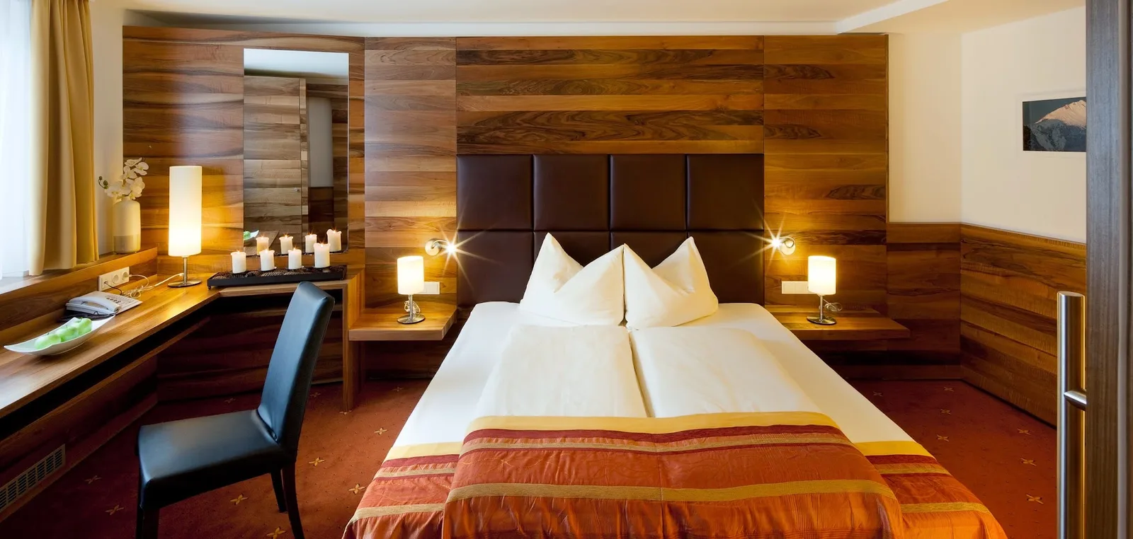Hotelzimmer mit großflächiger Holzvertäfelung, gepolstertem Kopfteil und Doppelbett